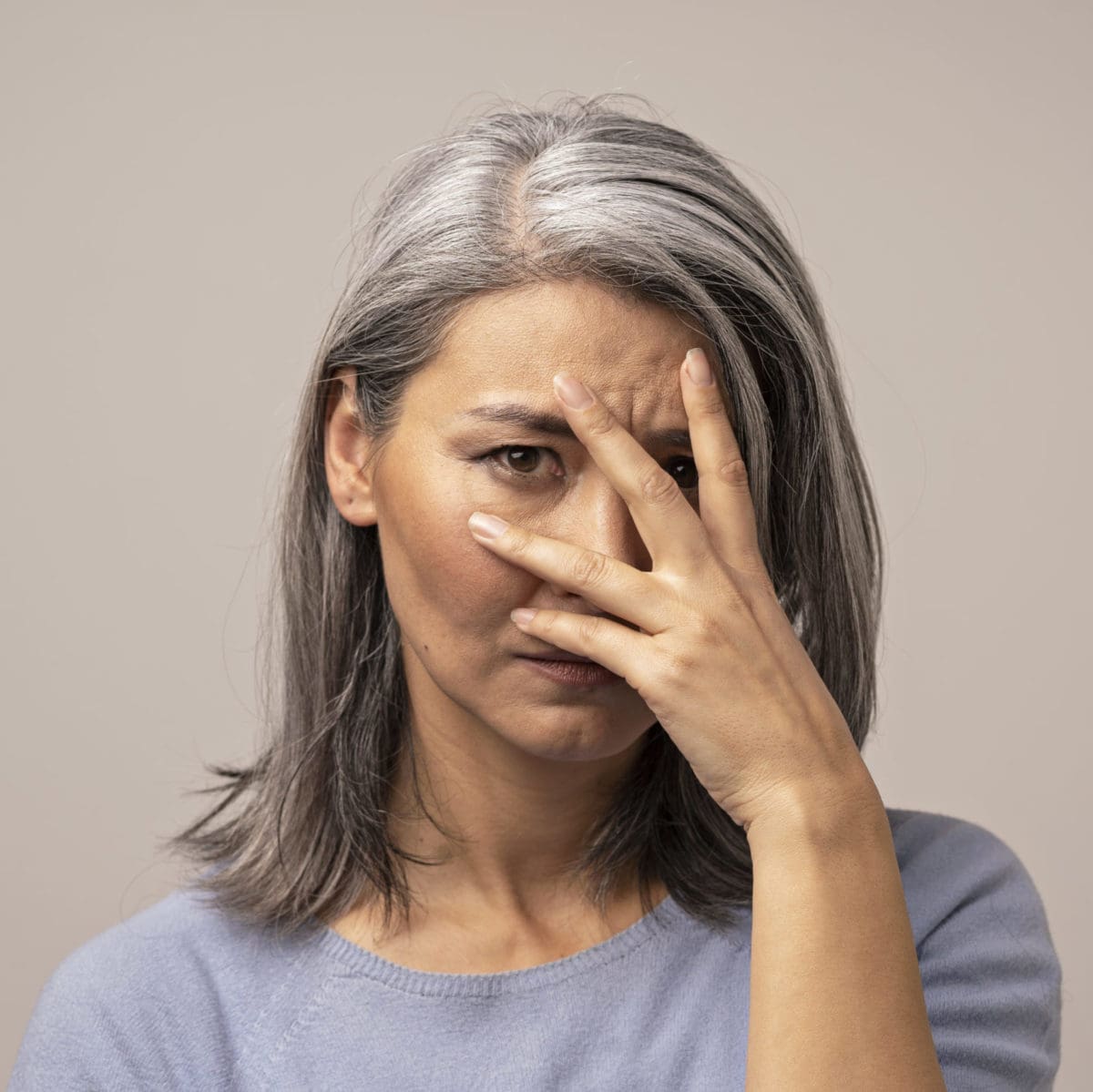 Elderly woman covering her face with one hand, appearing distressed about dental issues.