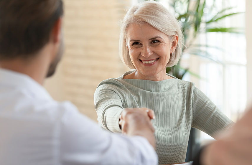 Elderly woman shaking hands and smiling, satisfied with dental services.