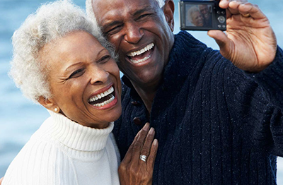 Elderly man taking a selfie with his wife, both displaying healthy smiles.